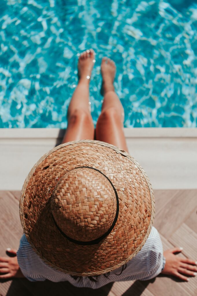 Fille de dos avec un chapeau de paille au bord e la piscine