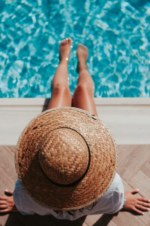 Fille de dos avec un chapeau de paille au bord e la piscine